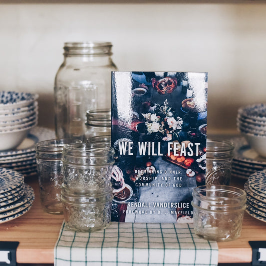 Table setting with blue and white patterned dishes, glasses, and a book titled 'We Will Feast'.