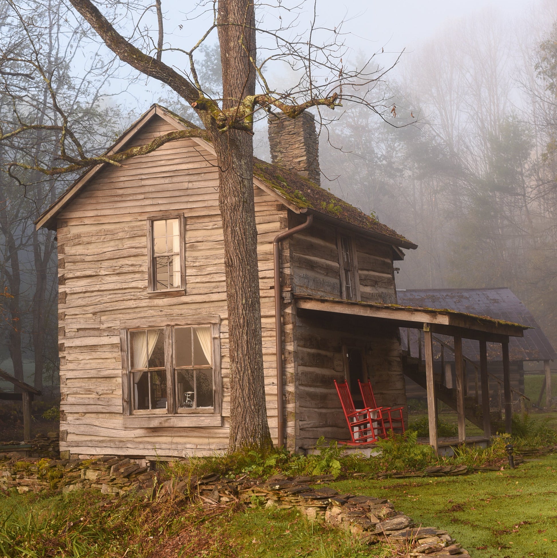 Old wooden cabin in a foggy, natural setting with a red chair on the porch.