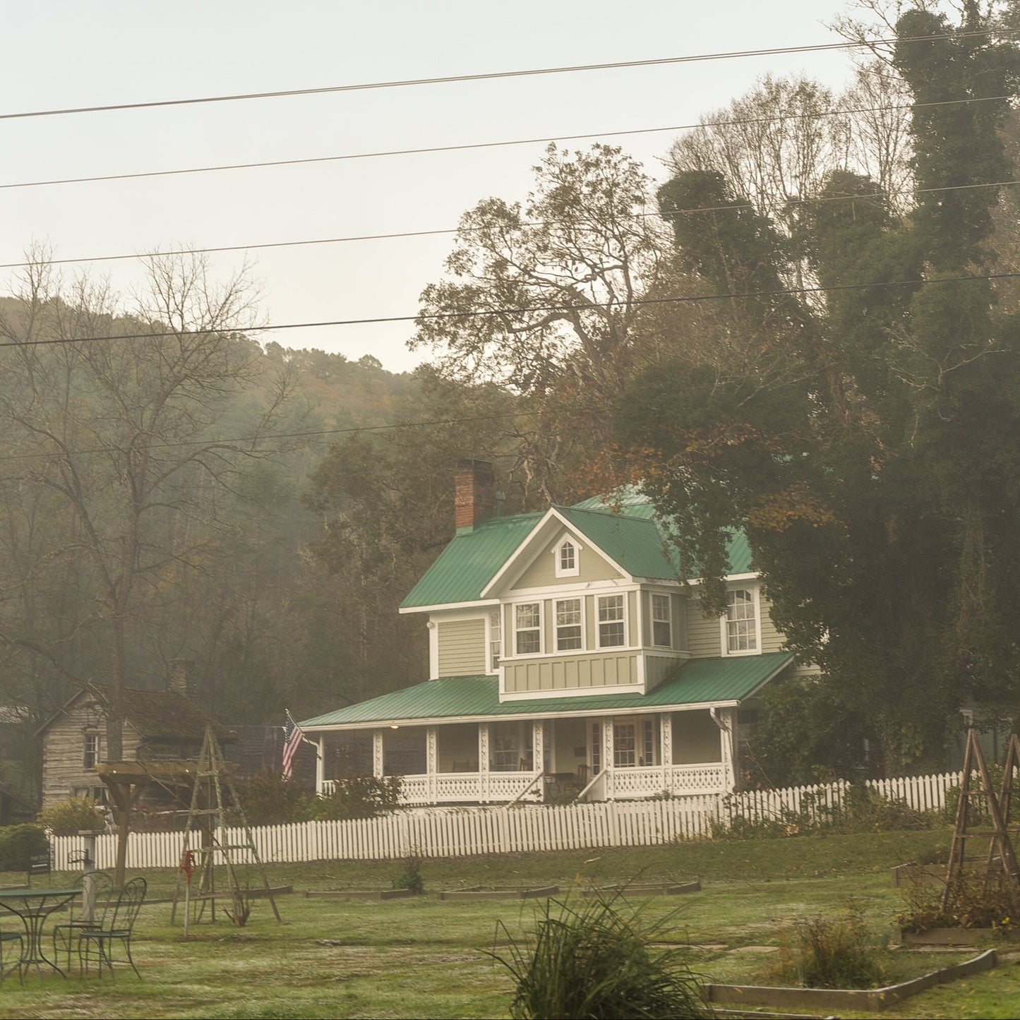 White house with a green roof in a rural setting with trees and power lines.