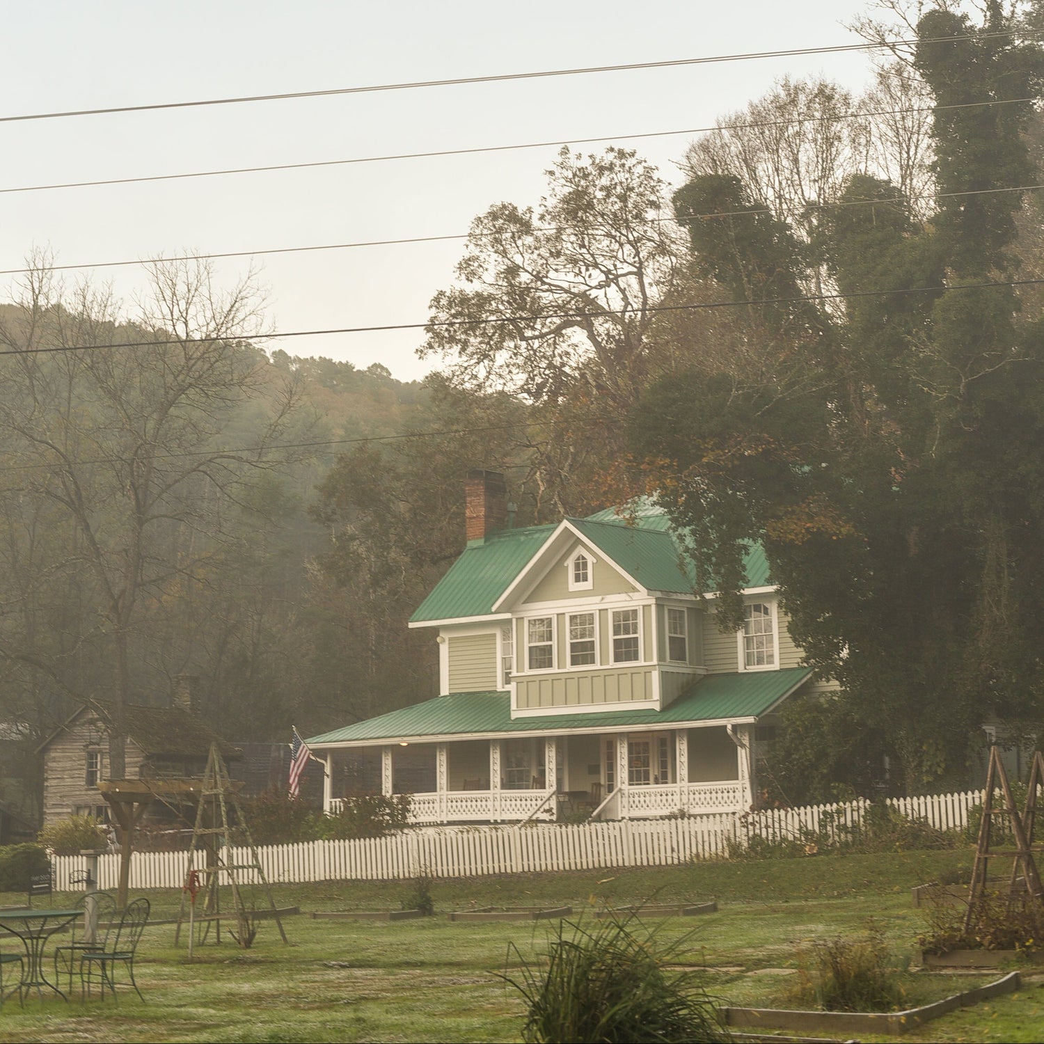 White house with a green roof in a rural setting with trees and power lines.
