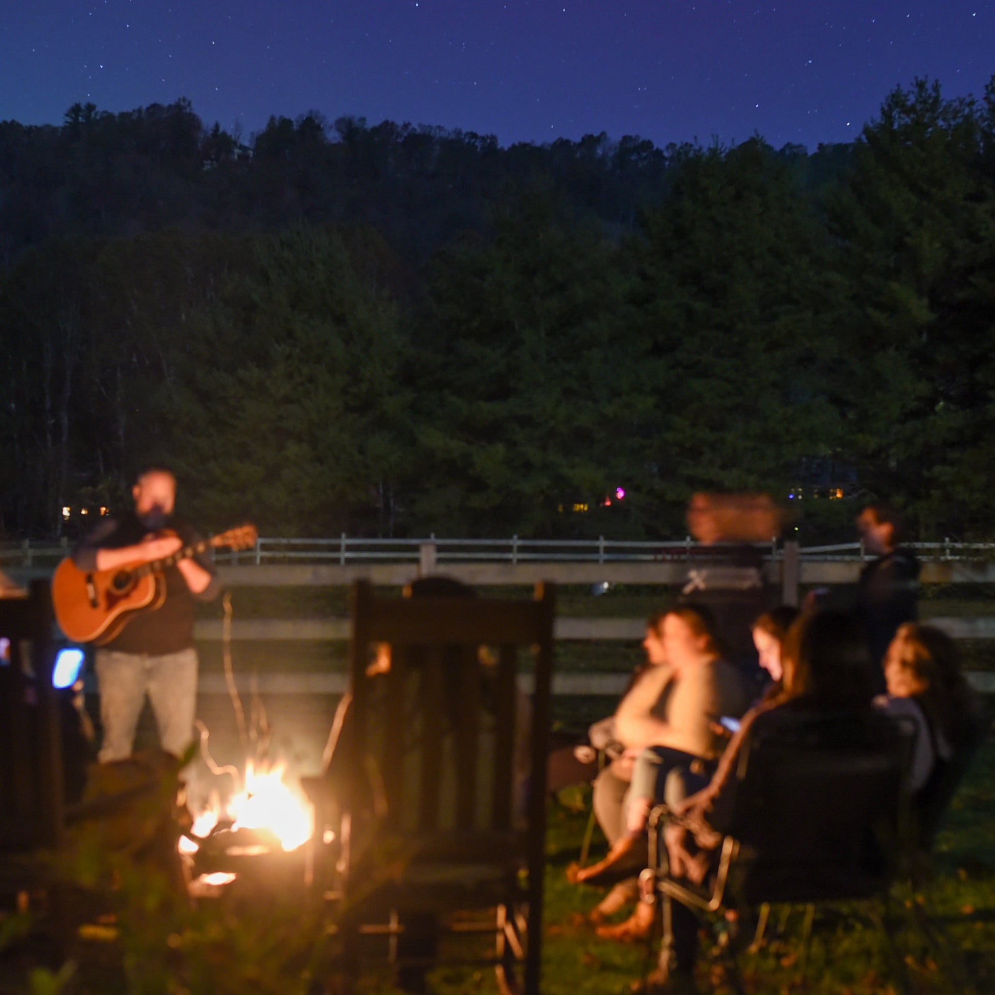 People gathered around a campfire at night with stars visible in the sky.
